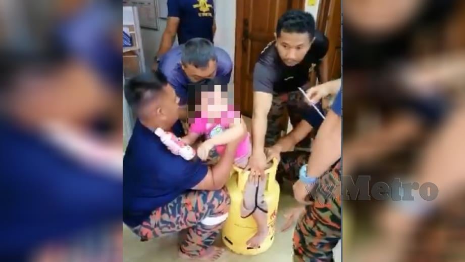 Anggota bomba memujuk kanak-kanak perempuan yang tersangkut kaki pada bahagian atas tong gas dalam kejadian di Perai pada Isnin lalu. Foto Ihsan JBPM
