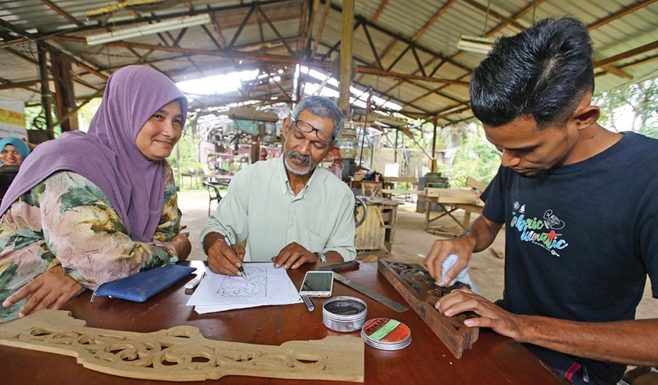 RAMLI (tengah) ditemani, Maimunah ketika membuat lakaran, manakala Mohd Amirul menggilap produk yang siap.