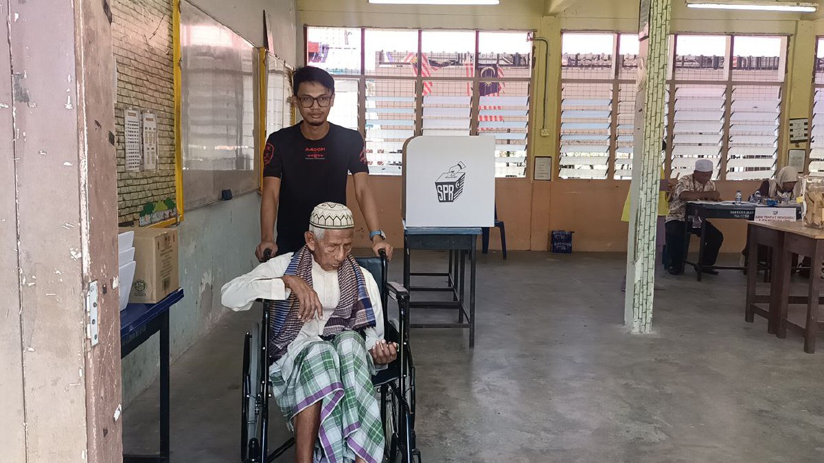 MOHD Izad membantu datuknya, Wan Ismail Wan Seman untuk mengundi di SMK Kampung Laut. FOTO Siti Rohana Idris.