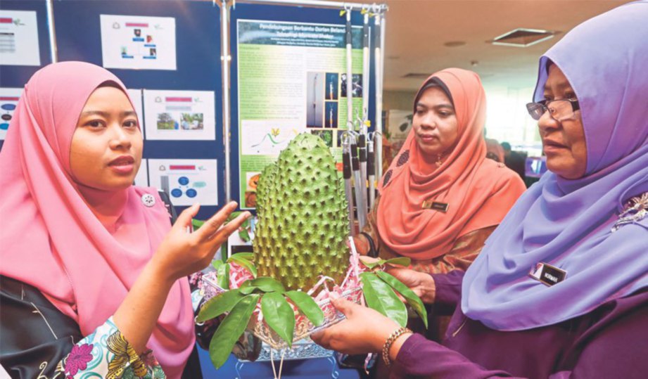 PELAJAR Latihan Industri Hortikultur Ayer Hitam, Johor, Nur Amirah Zaini (kiri) menunjukkan buah durian Belanda yang dihasilkan melalui inovasi muricata shaker kepada pengunjung.