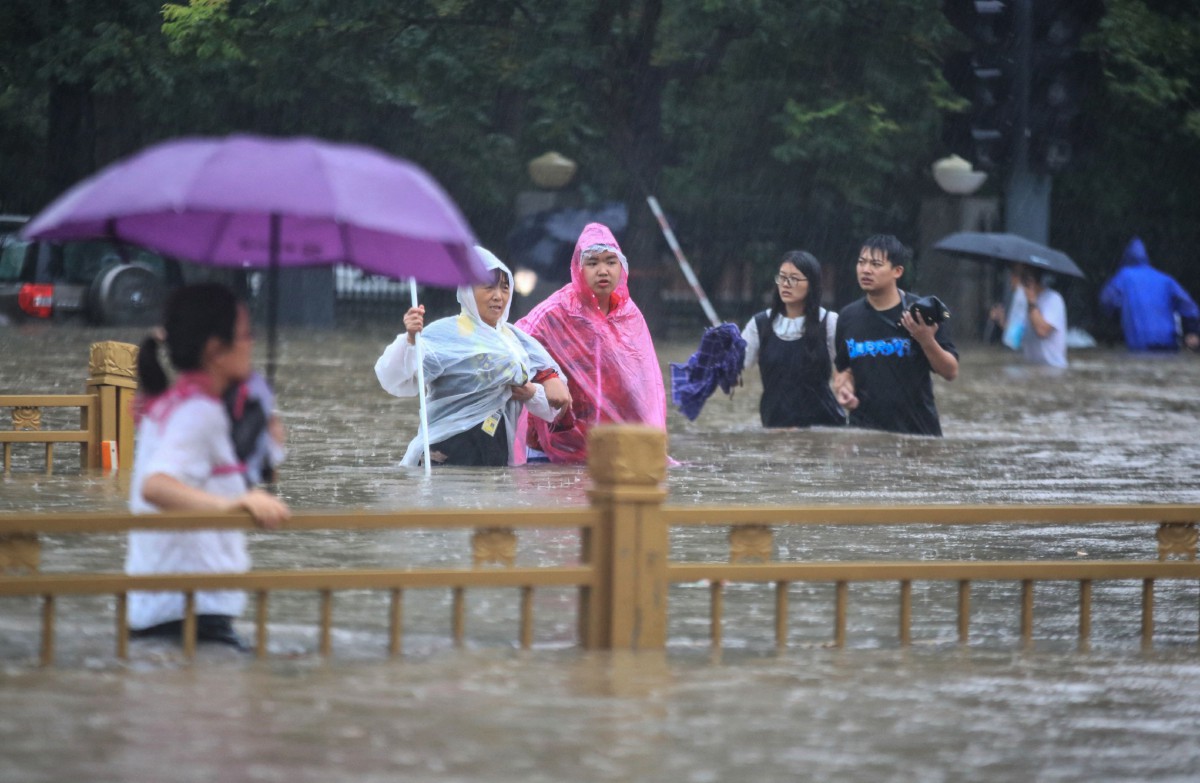 PENDUDUK berpayung meredah banjir di Zhengzhou, Henan. FOTO AFP.