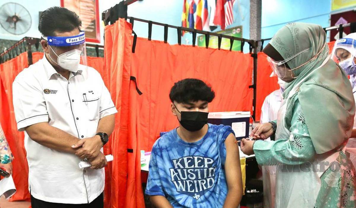 WAN Aqif Nafis (tengah) menerima suntikan vaksin dari Pengarah Kesihatan Negeri, Dr Kasemani (kanan)  menerusi Program Imunisasi Covid-19 Kebangsaan (Remaja) di SMK Sultan Sulaiman. FOTO Ghazali Kori