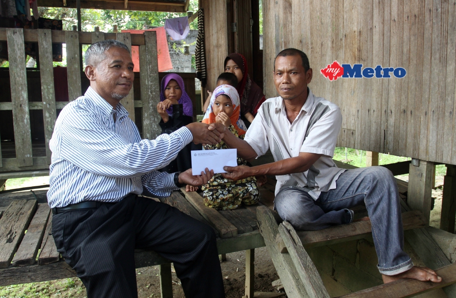 Nik Mohd Azlan (kiri) menyampaikan bantuan zakat kepada Sayuti di Kampung Gual Tok Deh. FOTO Nik Abdullah Nik Omar