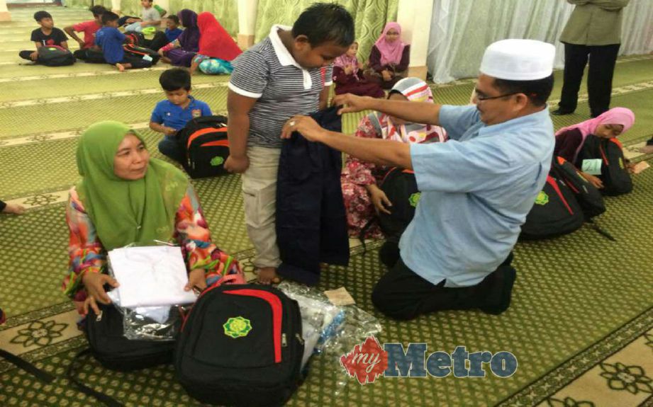 Ketua Pegawai Eksekutif Lembaga Zakat negeri Kedah, Zakaria Othman (kanan) cuba melihat kesesuaian seluar yang diberikan kepada kepada murid, Saiful Asraf Abdul Rahim (kanan) sambil diperhatikan oleh ibunya, Sharif Samad, 50 (kiri). FOTO Aizat Sharif